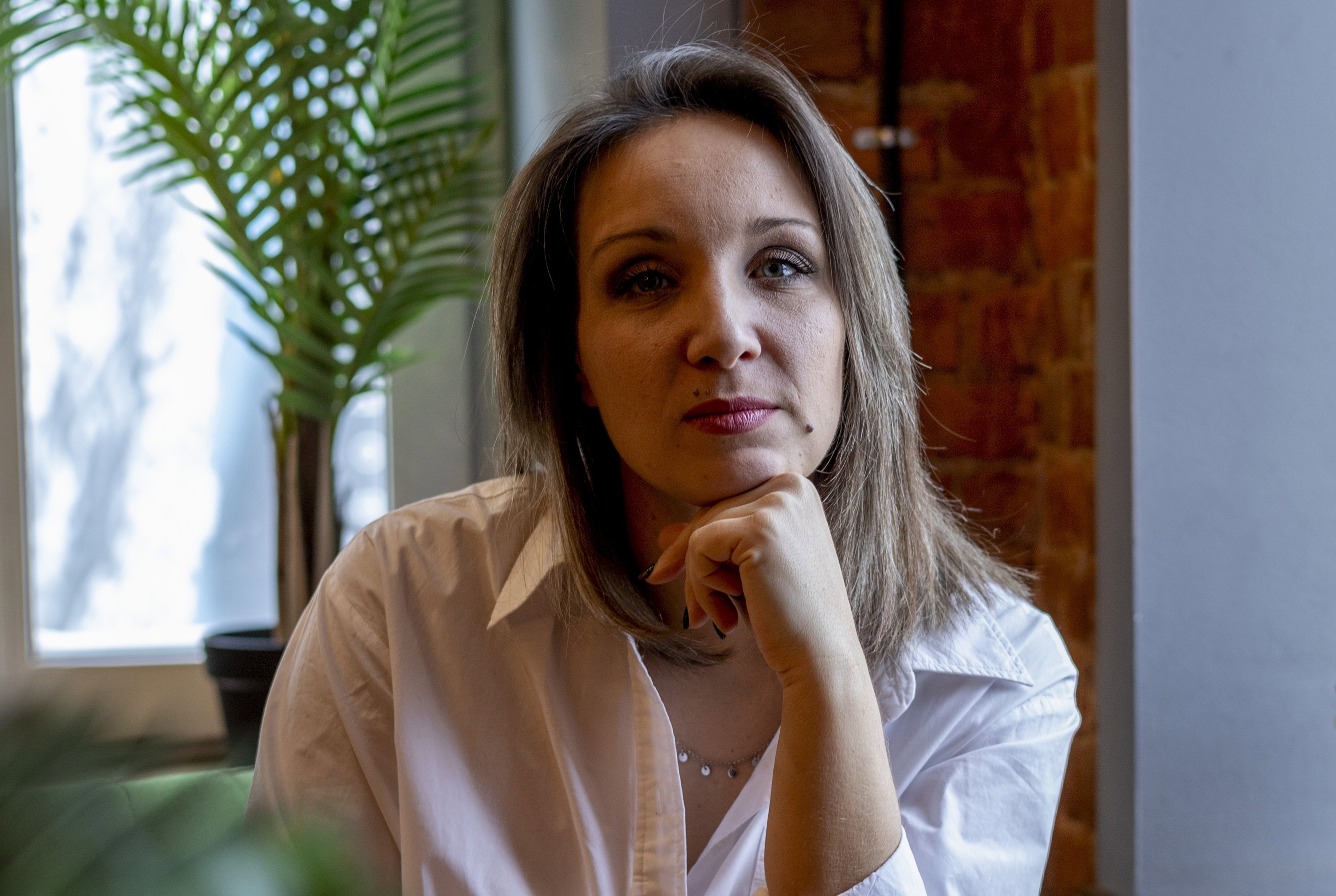 kobieta w wieku 35 plus w jasnej koszuli siedzi w lokalu smutna i zamyślona