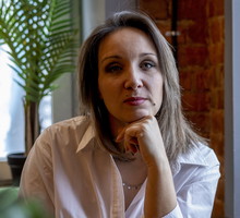 kobieta w wieku 35 plus w jasnej koszuli siedzi w lokalu smutna i zamyślona
