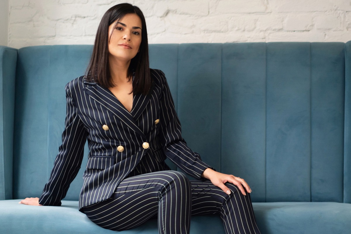 kobieta w wieku 30 plus ciemne włosy w dopasowanym garniturze siedzi na sofie z poważną miną