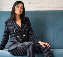 kobieta w wieku 30 plus ciemne włosy w dopasowanym garniturze siedzi na sofie z poważną miną