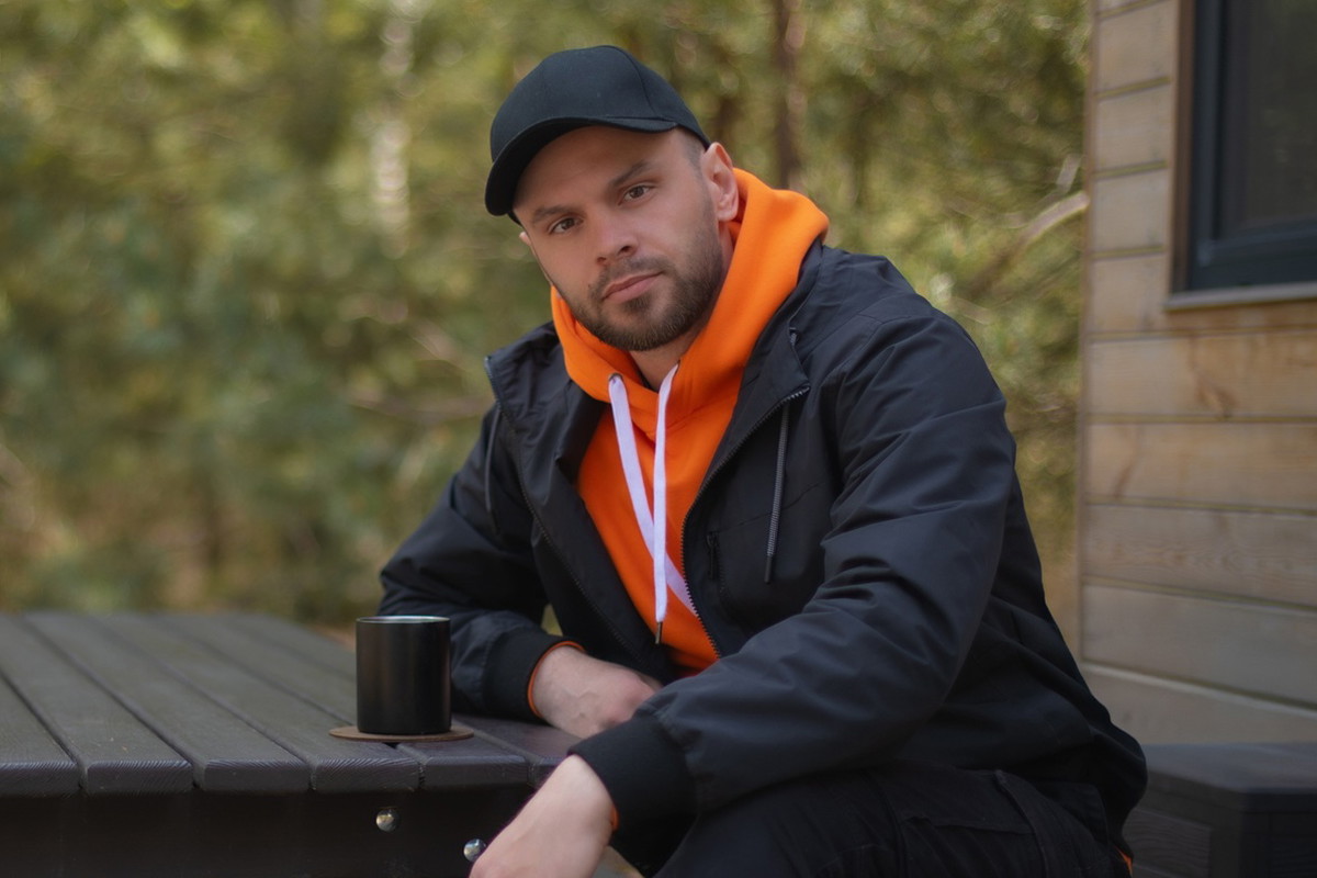 mężczyzna w wieku 30 plus w czapce z daszkiem siedzi przy drewnianej ławie z kubkiem herbaty zamyślony