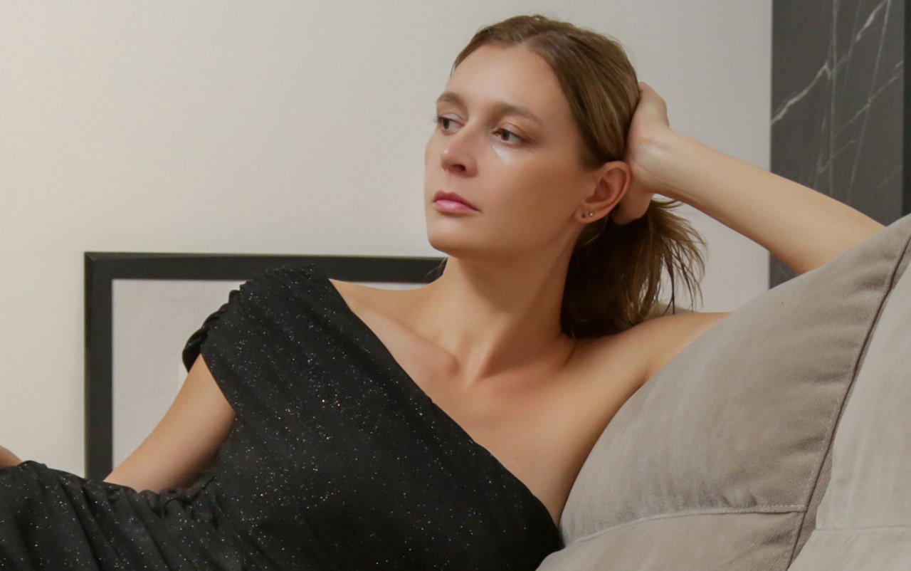 kobieta w wieku 30 plus w ciemnej mieniącej się sukni siedzi zamyślona i smutna na sofie