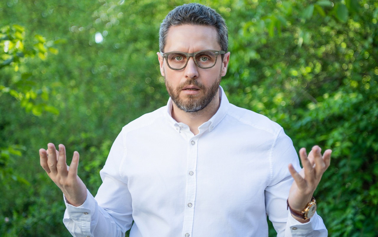 mężczyzna w wieku 40 plus w okularach i w białej koszuli stoi na zewnątrz zaskoczony i zdumiony