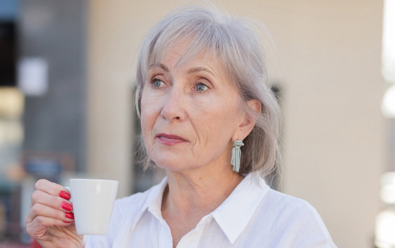 kobieta w wieku 60 plus siwe włosy z czerwonymi paznokciami elegancka pije espresso zamyślona i smutna