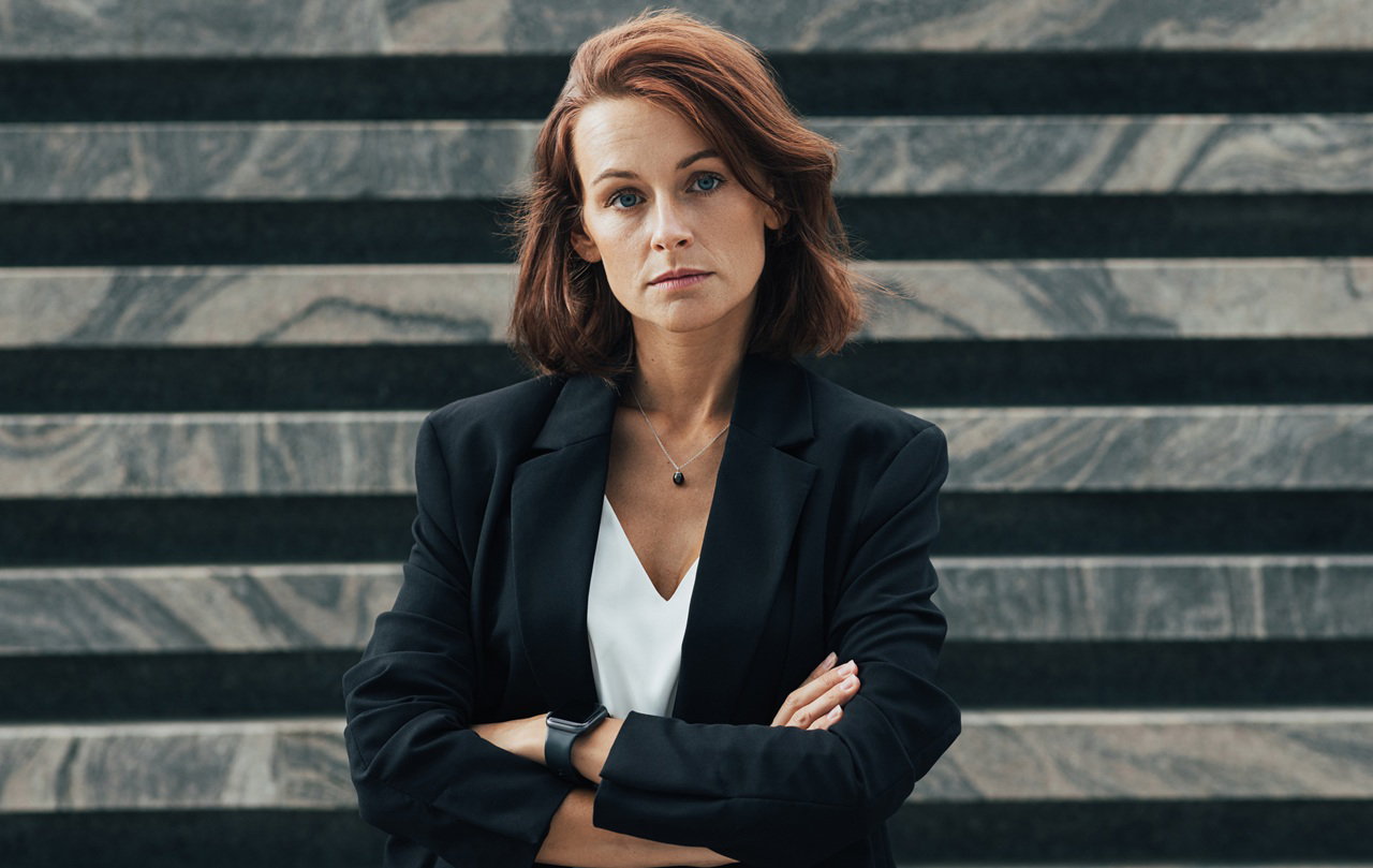 kobieta w wieku 35 plus poważna w czarnej marynarce i białym topie stoi na tle nowoczesnego budynku