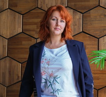 kobieta w wieku 40 plus rude włosy w granatowej marynarce stoi na tle drewnianej ściany zamyślona