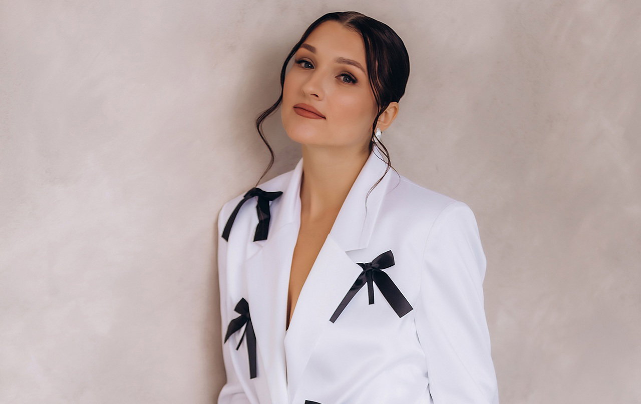 kobieta w wieku 30 plus w białym stroju z czarnymi kokardkami elegancka stoi smutna pod ścianą