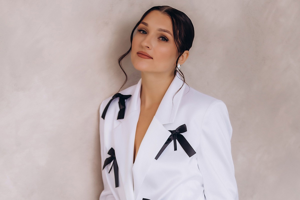 kobieta w wieku 30 plus w białym stroju z czarnymi kokardkami elegancka stoi smutna pod ścianą