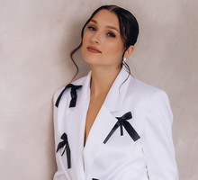 kobieta w wieku 30 plus w białym stroju z czarnymi kokardkami elegancka stoi smutna pod ścianą