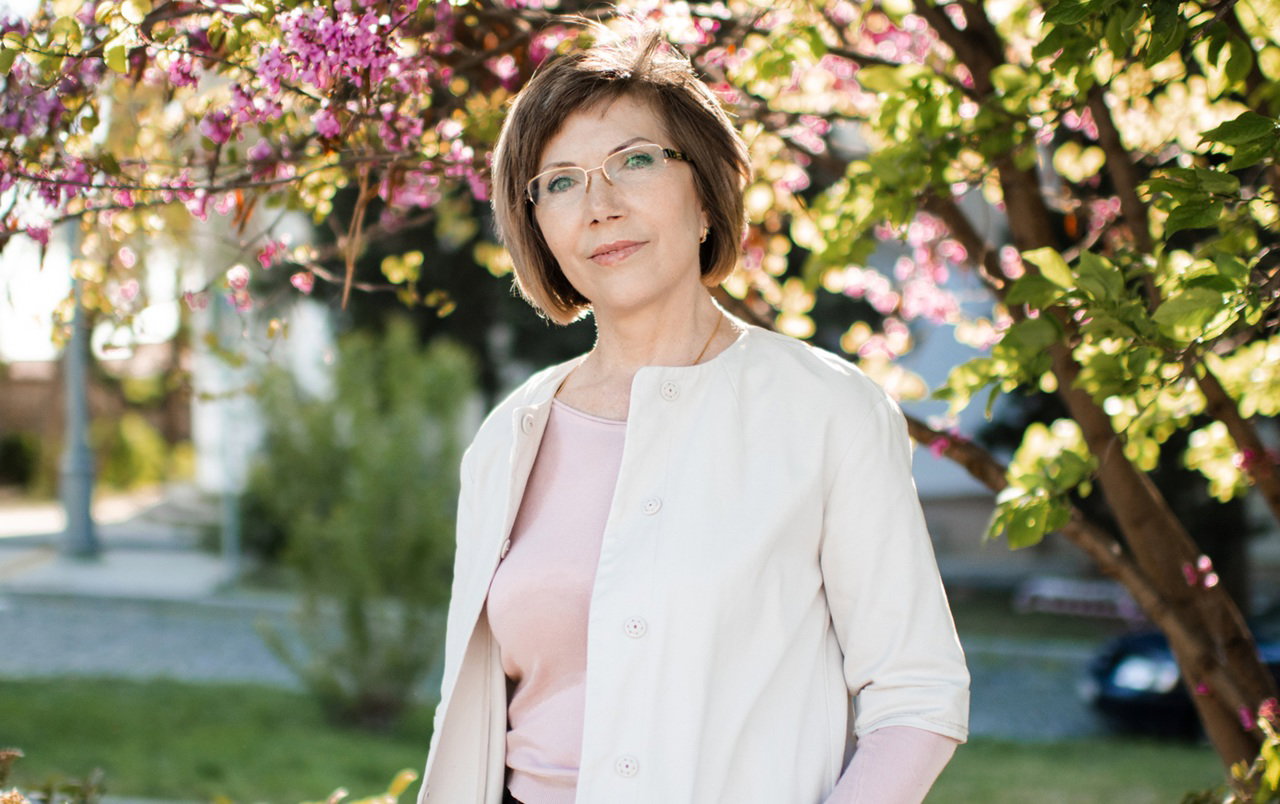 kobieta w wieku 50 plus w okularach stoi na tle kwitnących drzew smutna i zamyślona