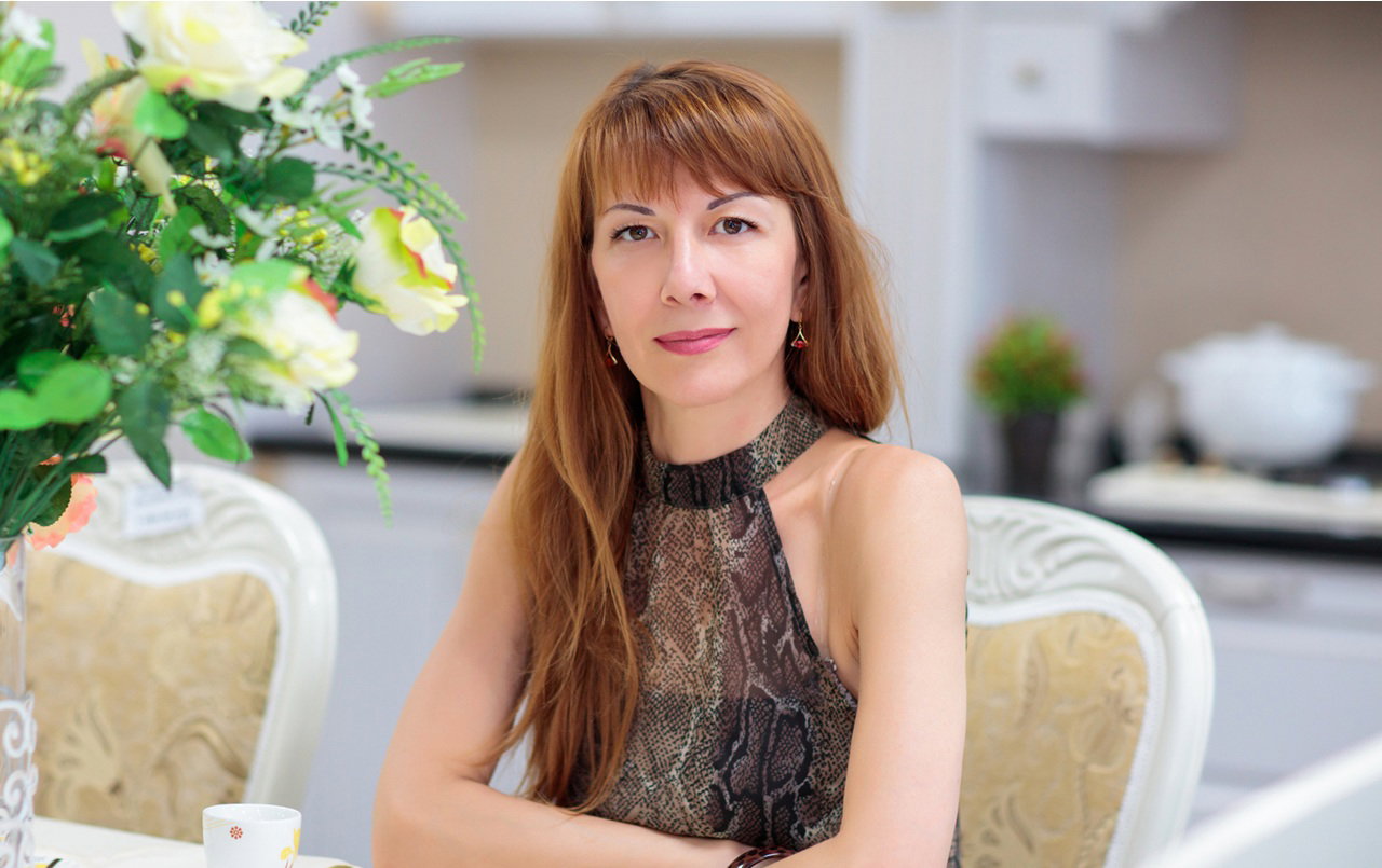 kobieta w wieku 35 plus siedzi w restauracji przy stole i lekko się uśmiecha z satysfakcją