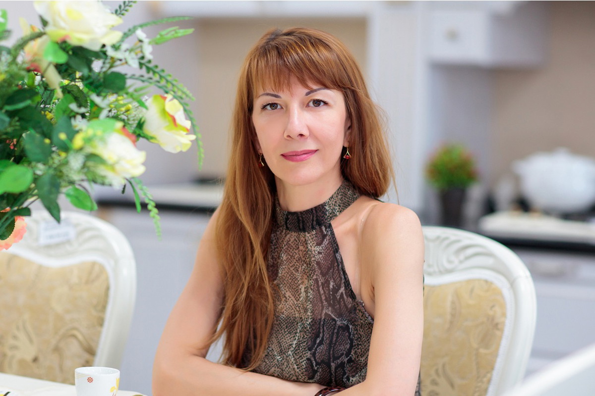 kobieta w wieku 35 plus siedzi w restauracji przy stole i lekko się uśmiecha z satysfakcją