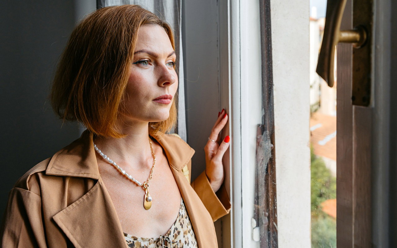 kobieta w wieku 30 plus rude włosy stoi w płaszczu przy oknie zamyślona i smutna