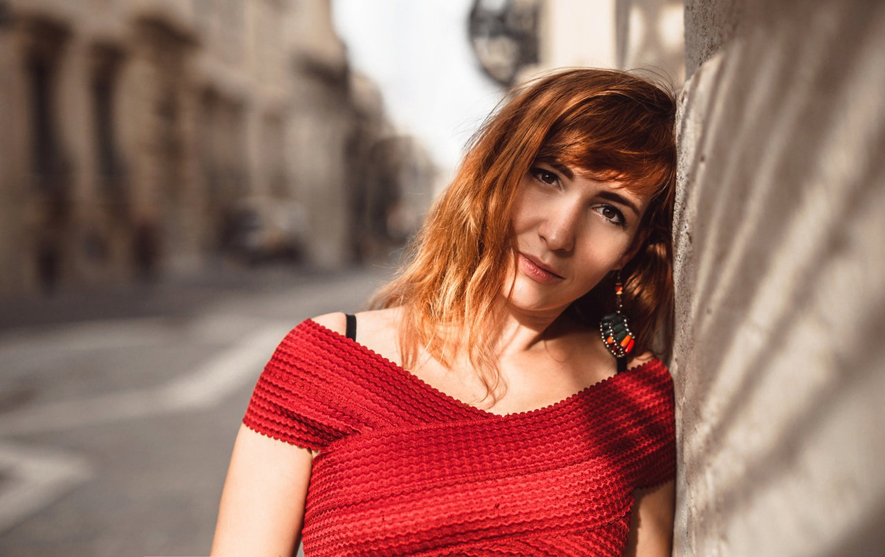 kobieta w wieku 30 plus w czerwonej sukience stoi na ulicy włoskiego miasta rozmarzona