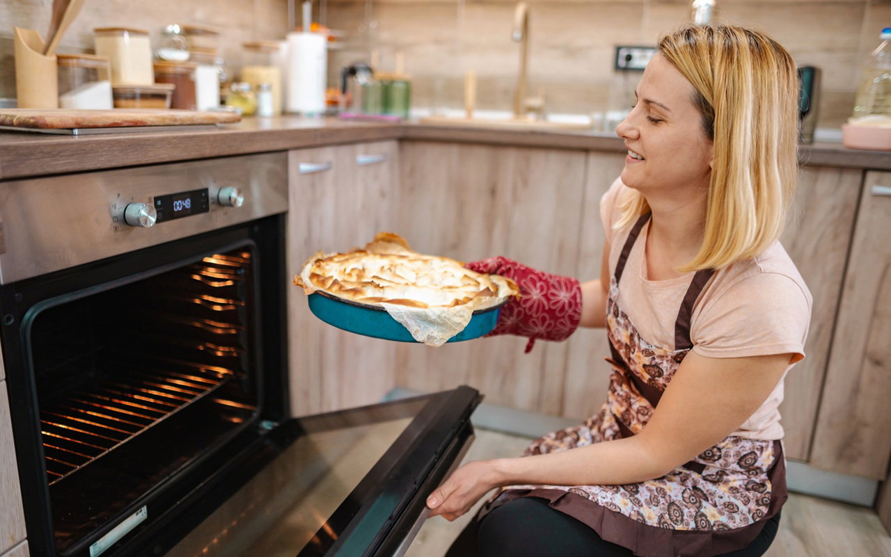 kobieta w wieku 35 plus wyciąga ciasto z piekarnika zadowolona