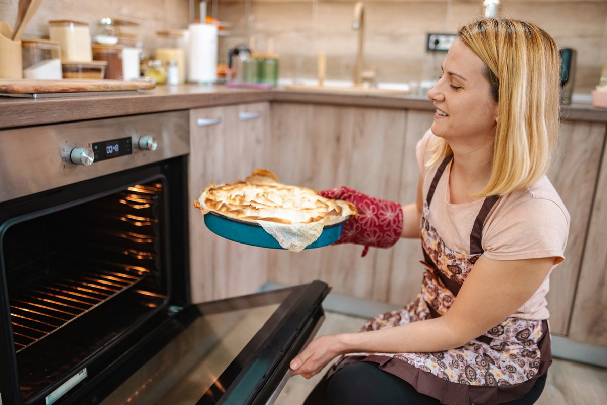 kobieta w wieku 35 plus wyciąga ciasto z piekarnika zadowolona