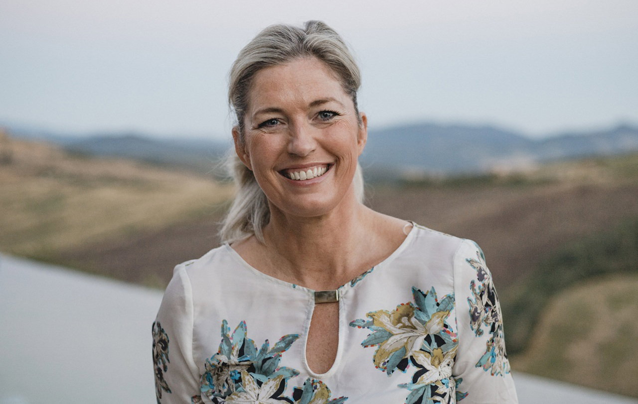 kobieta w  wieku 40 plus w kwiecistej sukience stoi na tle włoskiego pejzażu uśmiechnięta