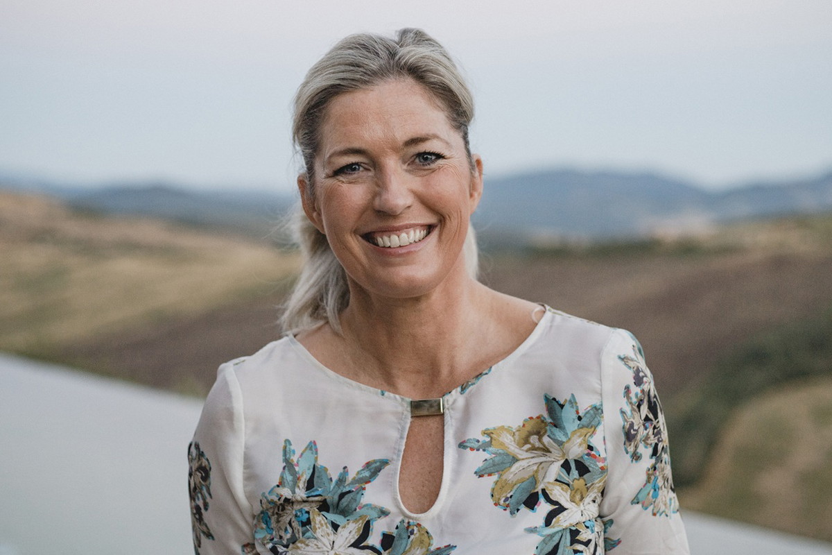 kobieta w wieku 40 plus w kwiecistej sukience stoi na tle włoskiego pejzażu uśmiechnięta