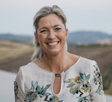 kobieta w wieku 40 plus w kwiecistej sukience stoi na tle włoskiego pejzażu uśmiechnięta