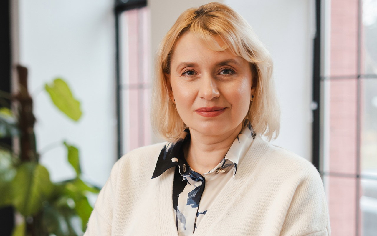 kobieta w wieku 45 plus blondynka stoi na tle okien dumna z siebie