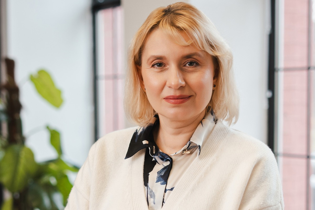 kobieta w wieku 45 plus blondynka stoi na tle okien dumna z siebie