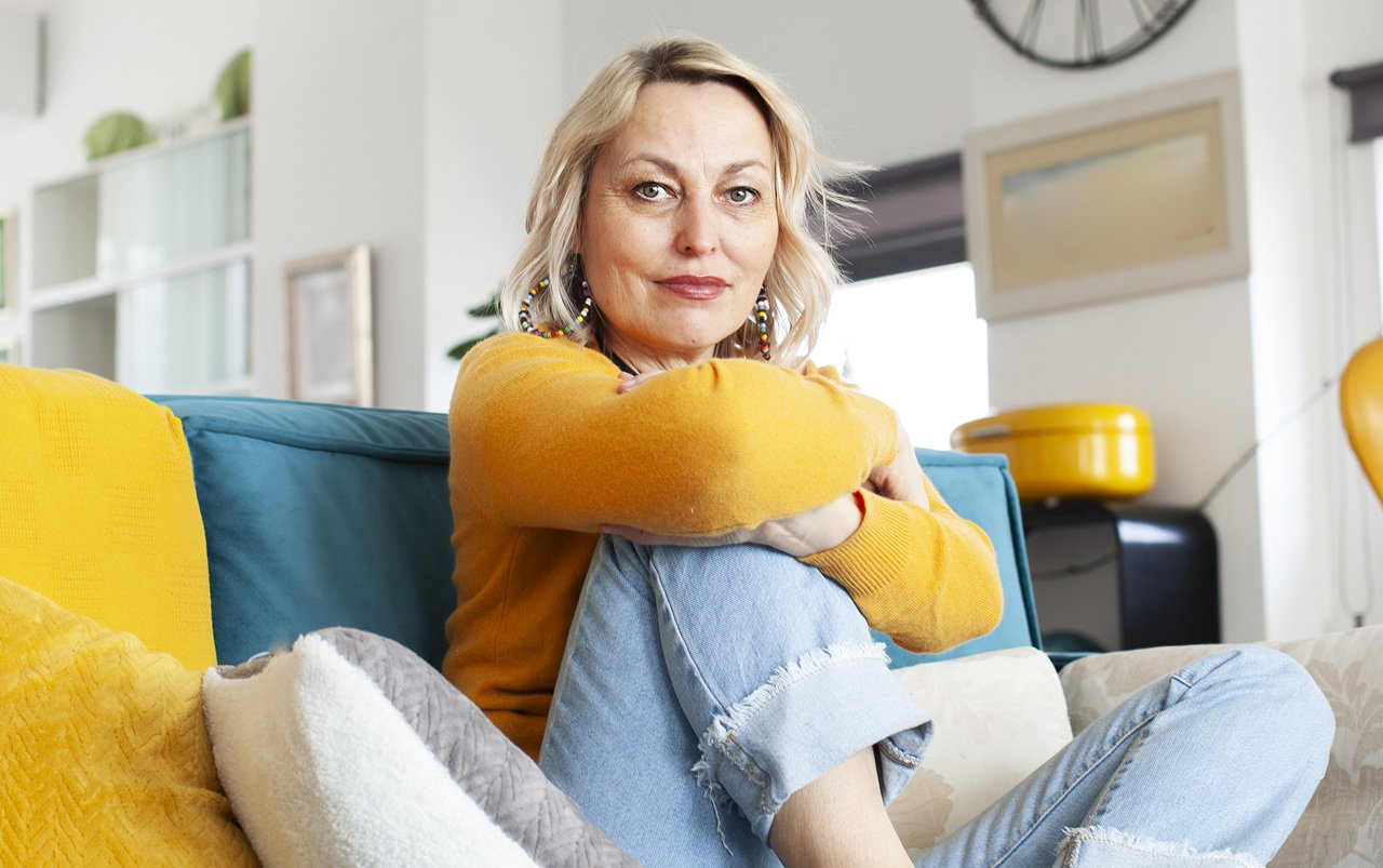 kobieta w wieku 50 plus blondynka siedzi na kanapie z poważną miną
