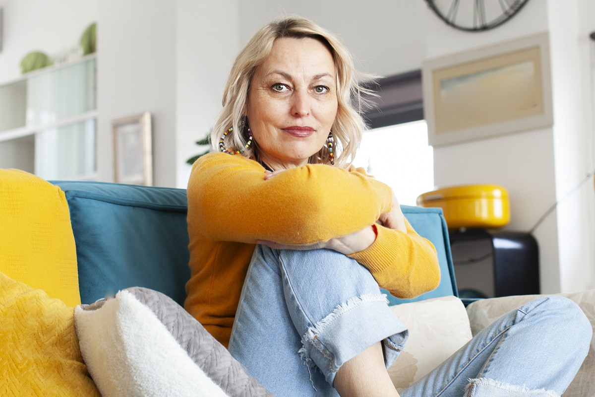 kobieta w wieku 50 plus blondynka siedzi na kanapie z poważną miną