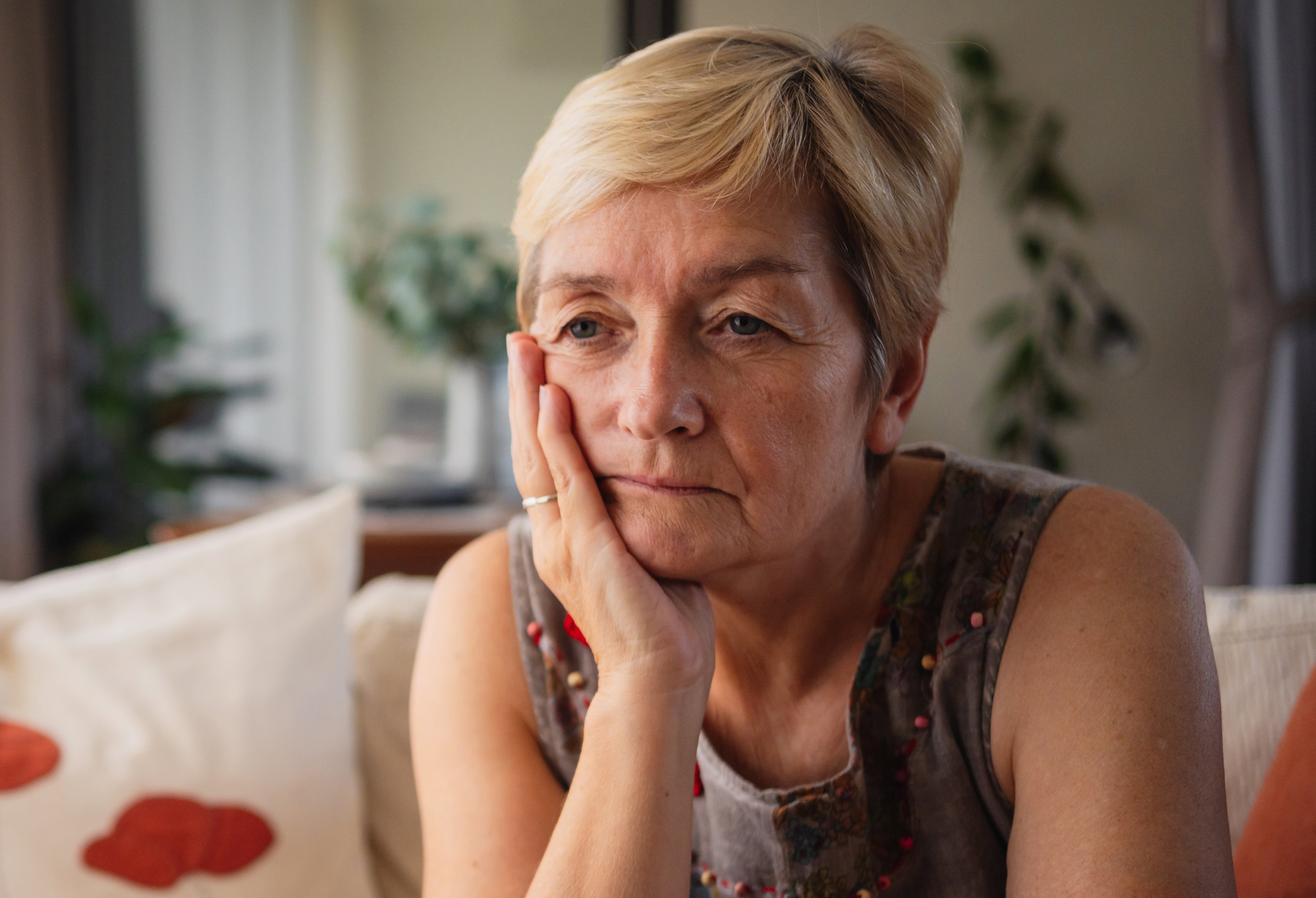 kobieta w wieku 60 plus siedzi na kanapie w salonie zmartwiona