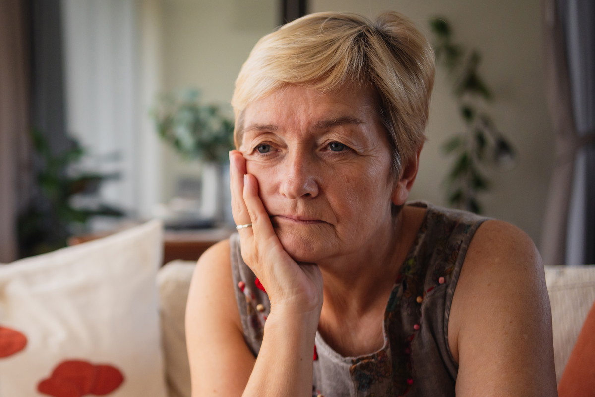 kobieta w wieku 60 plus siedzi na kanapie w salonie zmartwiona