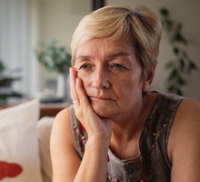 kobieta w wieku 60 plus siedzi na kanapie w salonie zmartwiona