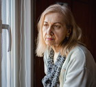 kobieta w wieku 60 plus z szalem na szyi siedzi smutna i zamyślona przy oknie