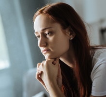kobieta w wieku 25 plus w białym t-shircie siedzi zamyślona na tle pokoju