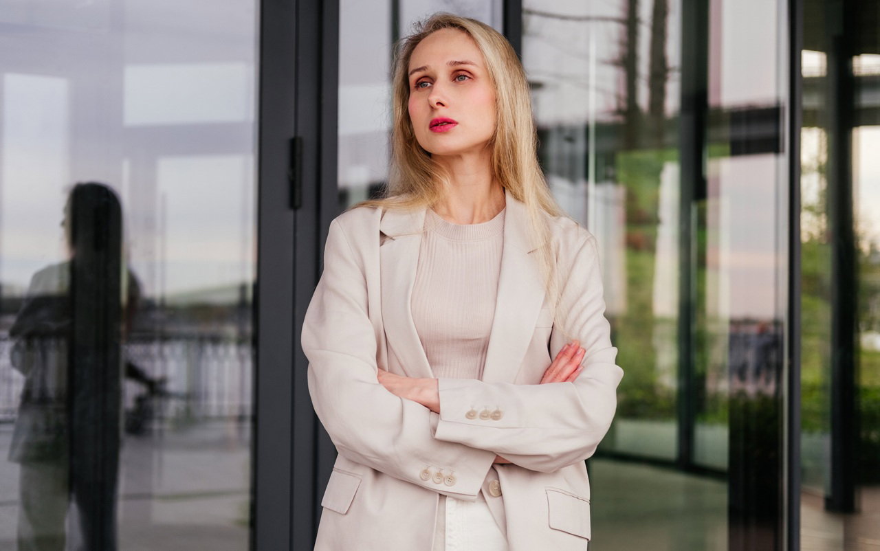 kobieta w wieku 30 plus blondynka stoi na tle szklanych drzwi budynku smutna