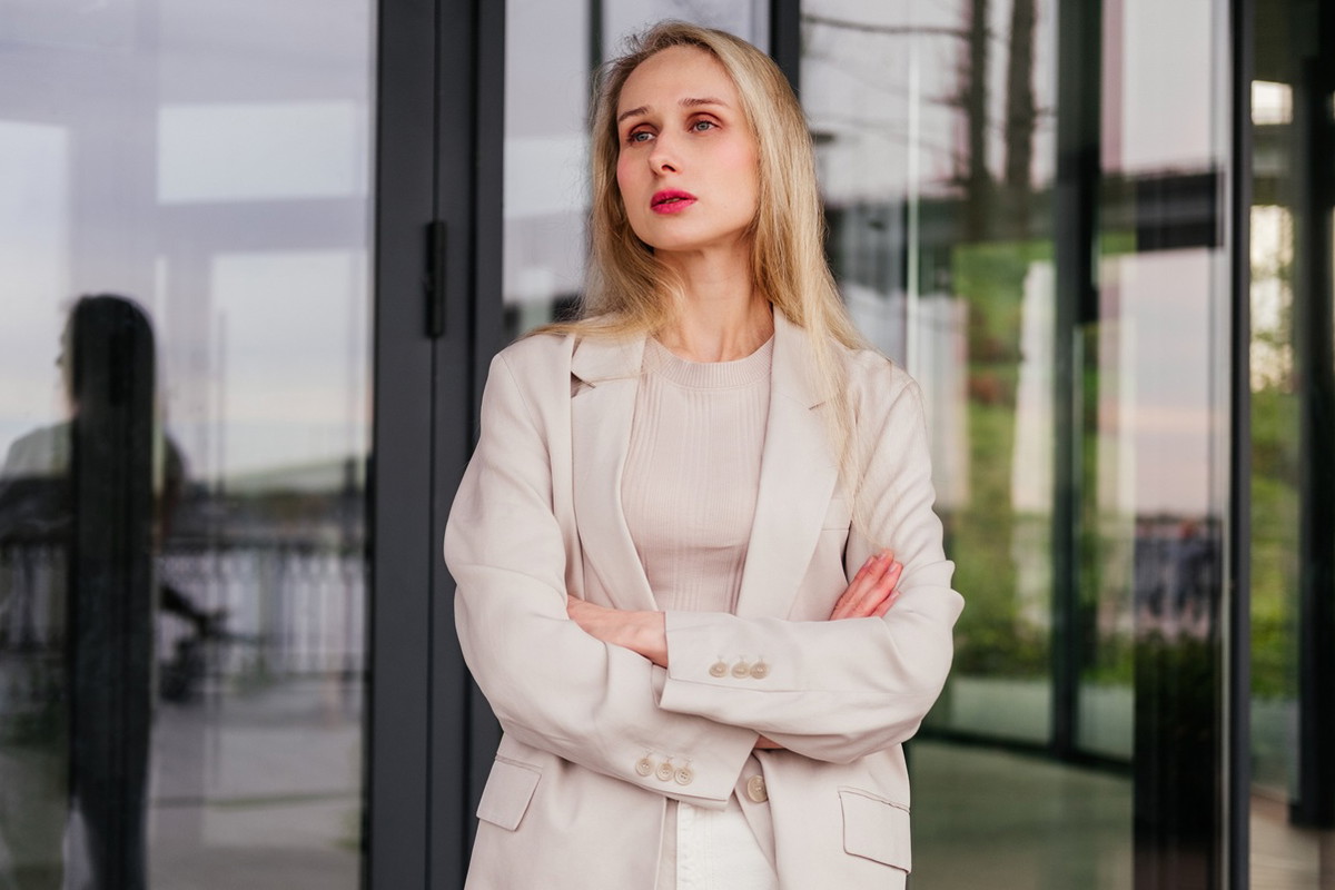 kobieta w wieku 30 plus blondynka stoi na tle szklanych drzwi budynku smutna