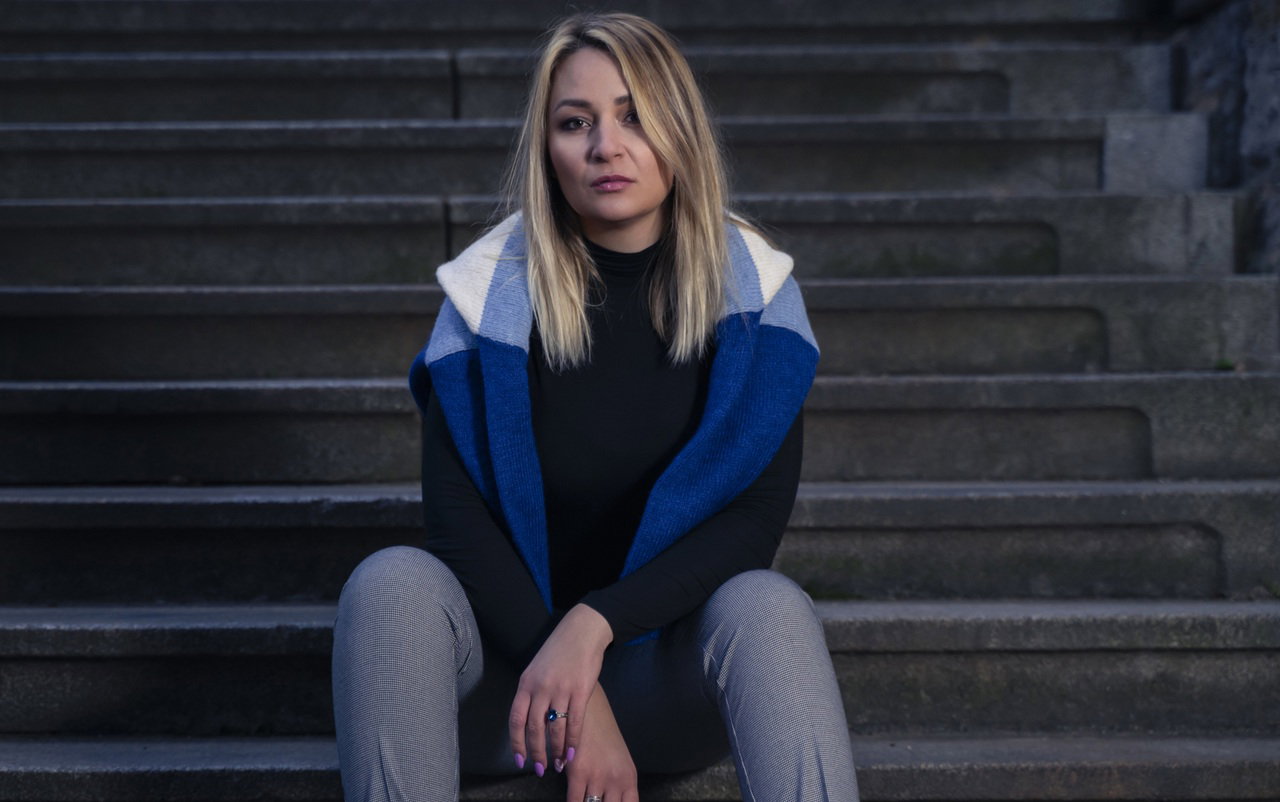 kobieta w wieku 30 plus blondynka ze swetrem na ramionach siedzi na schodach smutna i zrezygnowana