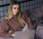 kobieta w wieku 30 plus siedzi na kanapie z laptopem i z poważną miną