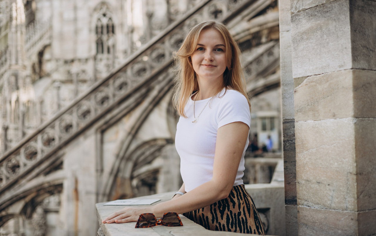 kobieta w wieku 30 plus stoi na tle Katedry Duomo w Mediolanie we Włoszech i lekko się uśmiecha