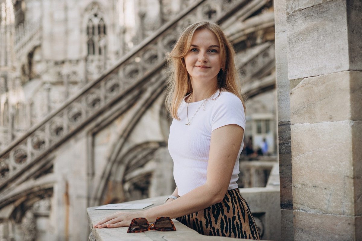 kobieta w wieku 30 plus stoi na tle Katedry Duomo w Mediolanie we Włoszech i lekko się uśmiecha