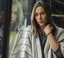kobieta w wieku 30 plus stoi przy oknie i rozmyśla ze zmartwioną miną