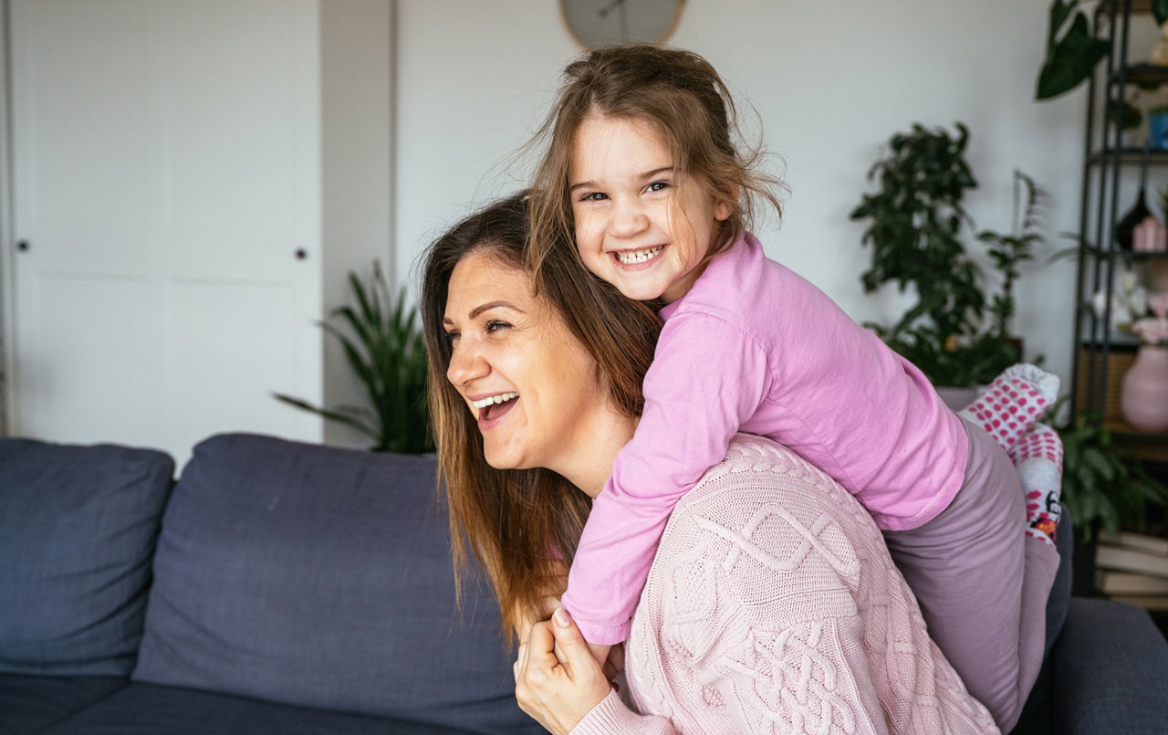 kobieta w wieku 35 plus bawi się z córką w salonie i obie śmieją się wesoło