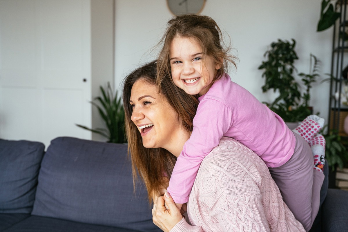 kobieta w wieku 35 plus bawi się z córką w salonie i obie śmieją się wesoło