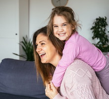 kobieta w wieku 35 plus bawi się z córką w salonie i obie śmieją się wesoło