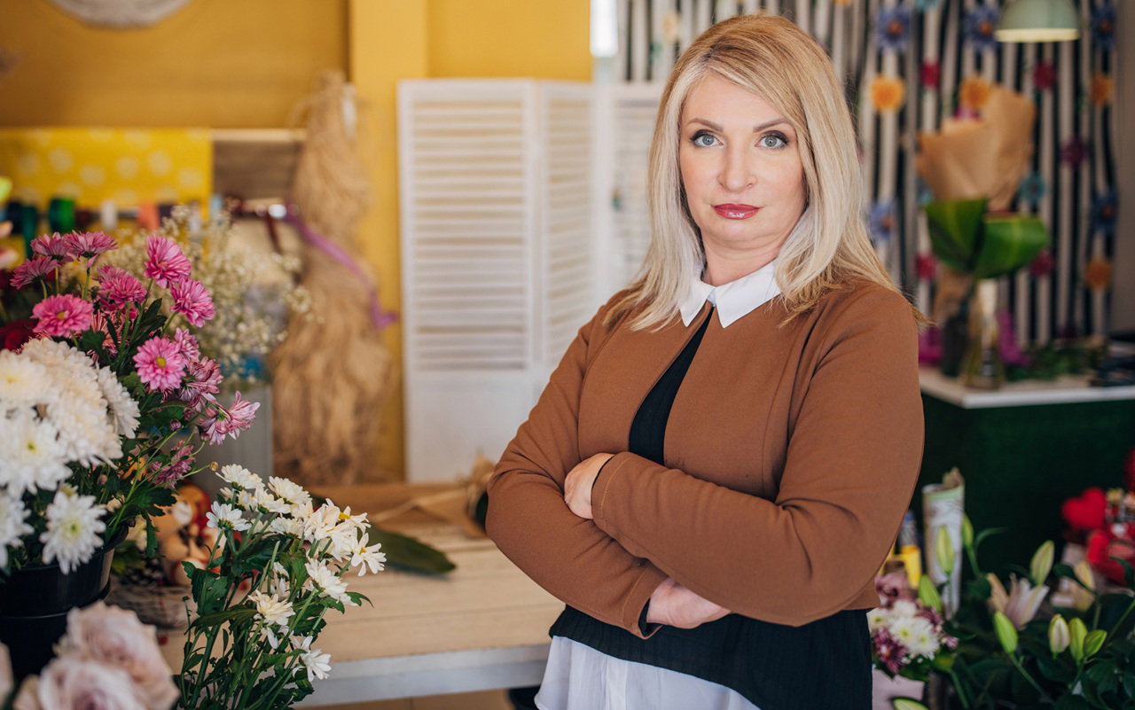 kobieta w wieku 40 plus blondynka stoi w kwiaciarni z nadąsaną mina