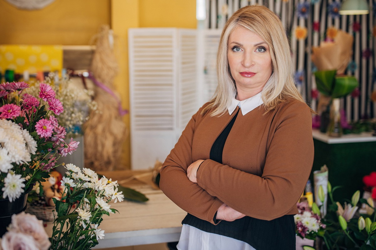 kobieta w wieku 40 plus blondynka stoi w kwiaciarni z nadąsaną mina