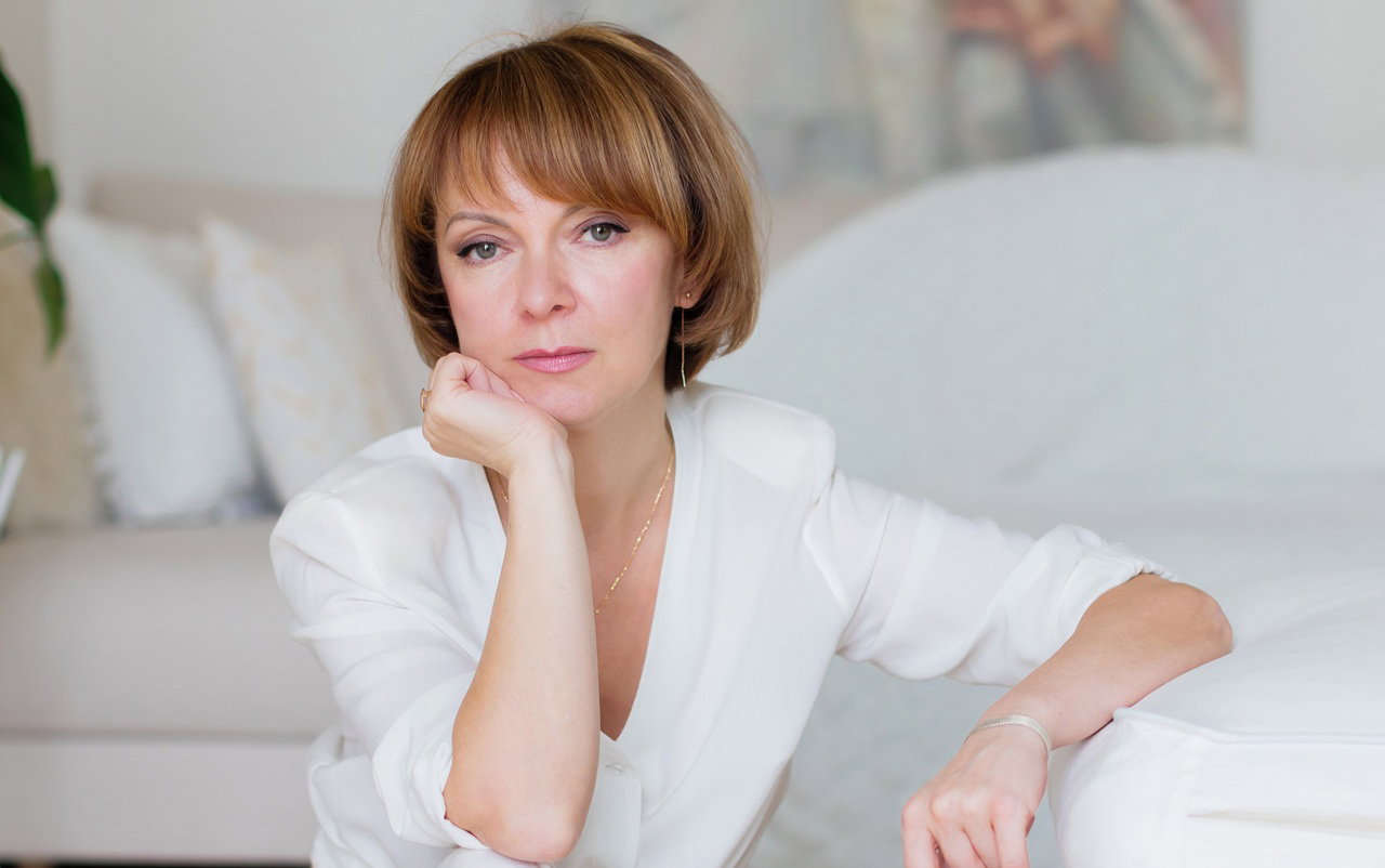 kobieta w wieku 45 plus w białym stroju siedzi w eleganckim wnętrzu smutna i zamyślona