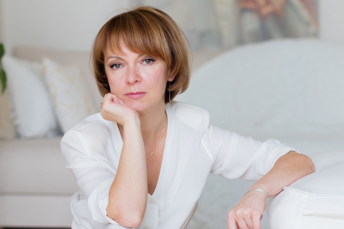 kobieta w wieku 45 plus w białym stroju siedzi w eleganckim wnętrzu smutna i zamyślona