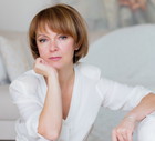 kobieta w wieku 45 plus w białym stroju siedzi w eleganckim wnętrzu smutna i zamyślona