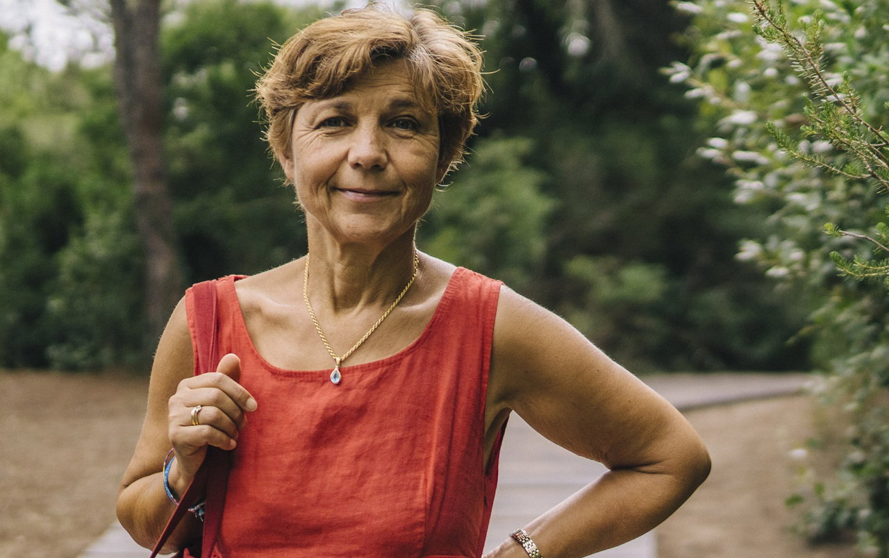 kobieta w wieku 60 plus w lnianej sukience stoi przy piniach i uśmiecha się kpiąco