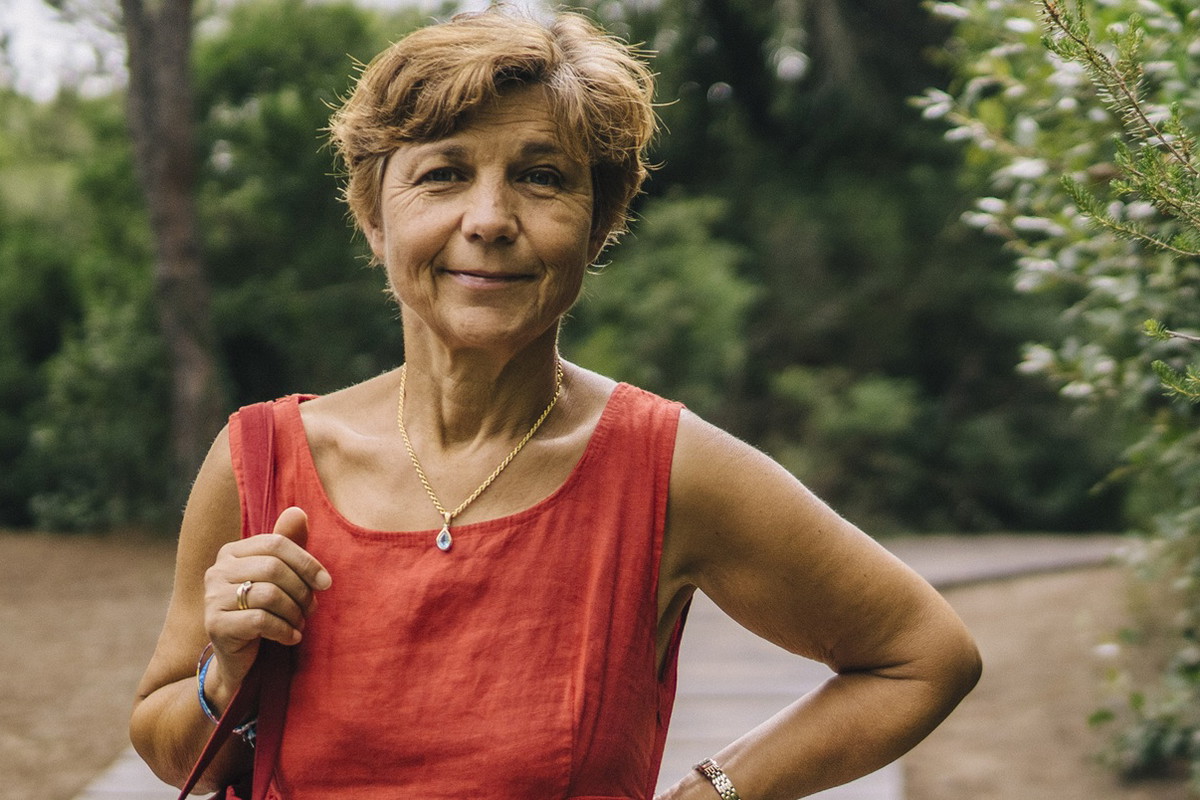 kobieta w wieku 60 plus w lnianej sukience stoi przy piniach i uśmiecha się kpiąco