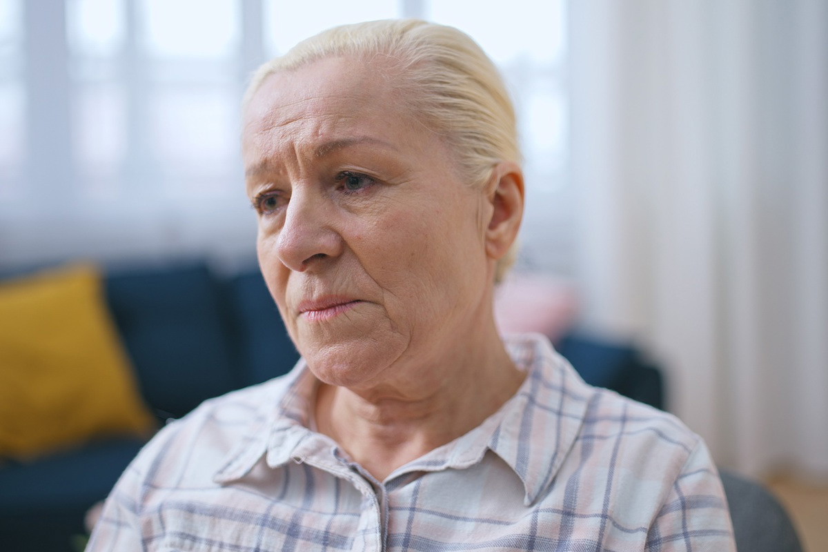 kobieta w wieku 65 plus blond włosy siedzi na kanapie w salonie załamana i smutna